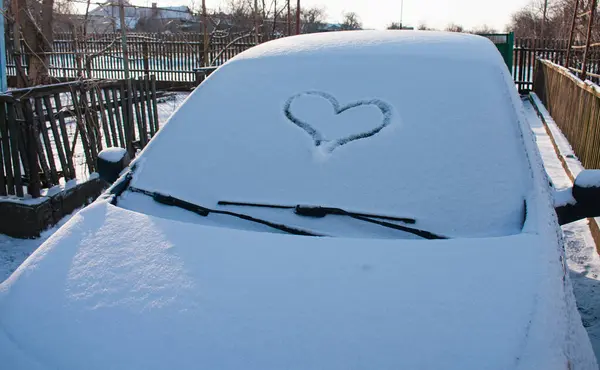 A heart drawn in the snow on the windshield of a car.