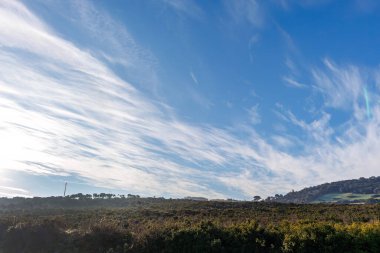 Bulutlu mavi gökyüzüne karşı çayır ve tepelerin manzarası