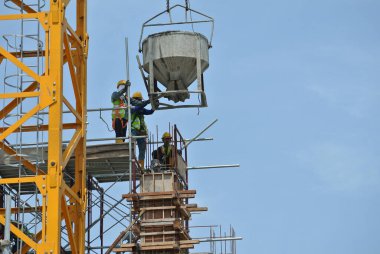 JOHOR, MALAYSIA - 12 Mayıs 2016: İnşaat alanındaki sütun biçimindeki çalışmalara beton kova döken bir grup inşaat işçisi.  