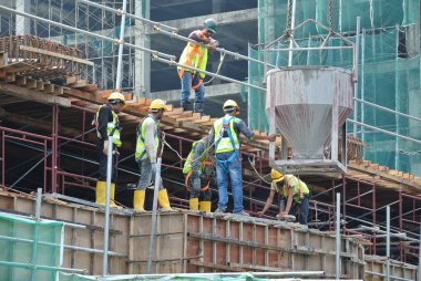 JOHOR, MALAYSIA - 12 Mayıs 2016: İnşaat alanındaki sütun biçimindeki çalışmalara beton kova döken bir grup inşaat işçisi.  
