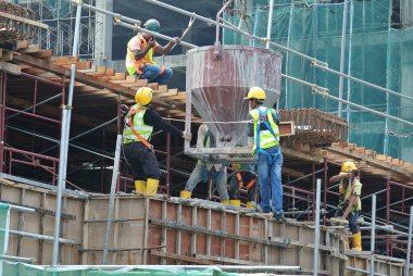 JOHOR, MALAYSIA - 12 Mayıs 2016: İnşaat alanındaki sütun biçimindeki çalışmalara beton kova döken bir grup inşaat işçisi.  