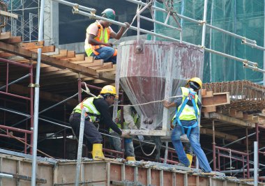 JOHOR, MALAYSIA - 12 Mayıs 2016: İnşaat alanındaki sütun biçimindeki çalışmalara beton kova döken bir grup inşaat işçisi.  