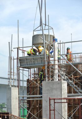 JOHOR, MALAYSIA - 12 Mayıs 2016: İnşaat alanındaki inşaat alanında zemine beton kova döken bir grup inşaat işçisi.  