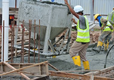 JOHOR, MALAYSIA - 12 Mayıs 2016: İnşaat alanındaki inşaat alanında zemine beton kova döken bir grup inşaat işçisi.  