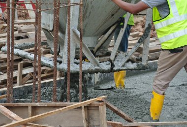 JOHOR, MALAYSIA - 12 Mayıs 2016: İnşaat çalışanları inşaat sahasının zemin kaplamasına beton kovayla çiğ beton döktü.  