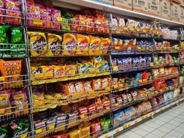JOHOR, MALAYSIA -APRIL 7, 2022: Selective focused on packed miscellaneous brand junk foods and snacks on the rack and display for sale in the supermarket. Each has its own price tag. 