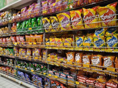 JOHOR, MALAYSIA -APRIL 7, 2022: Selective focused on packed miscellaneous brand junk foods and snacks on the rack and display for sale in the supermarket. Each has its own price tag. 
