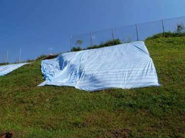 MELAKA, MALAYSIA - 6 Temmuz 2023: Yağmur suyunun neden olduğu kayalık erozyonunu önlemek için büyük bir plastik tabaka geçici eğim koruması olarak kullanılır.