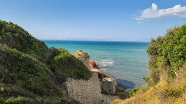 Arnavutluk sahilindeki gözlerden uzak bir koyda güzel bir panoramik manzara. Antik bir taş bina, güneşli bir yaz gününde İyon Denizi 'nin sakin mavi sularına tepeden bakan yeşil, bitki örtülü uçurumlara kurulmuştur..