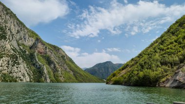 Arnavutluk Alpleri 'ndeki Koman Gölü' nün (Liqeni i Komanit) zümrüt sularını çevreleyen dramatik, dik uçurumlar ve kayalık dağların çarpıcı manzarası. Bu insan yapımı rezervuar muhteşem, fiyort benzeri manzarasıyla ünlüdür..