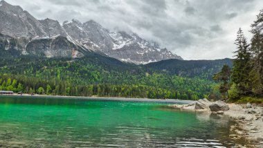 Eibsee Gölü 'nün canlı zümrüt suları kar kaplı Zugspitze dağıyla dramatik, bulutlu bir günde Almanya' nın Bavyera şehrinde