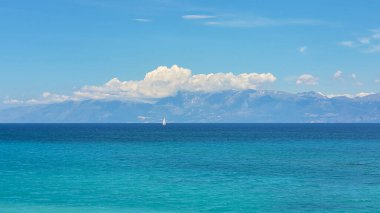 Turkuaz İyon Denizi 'nde yalnız bir yelkenli, Korfu' daki Kanal d 'Amour' dan izleniyor ve arka planda Arnavut dağları var.