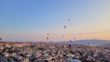Türkiye 'nin başkenti Kapadokya' daki Greme kasabasının mağara otelleri ve peri bacaları üzerinde uçan sıcak hava balonlarının nefes kesici gündoğumu manzarası.