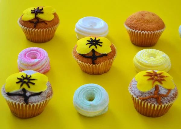 Rows of muffins decorated with powdered sugar and yellow flower shaped icing on a yellow background