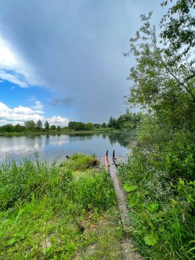 Kırsalda güzel küçük bir göl. Gökyüzünde bulutlarla güneşli bir gün. Rahatlamak için mükemmel bir yer.