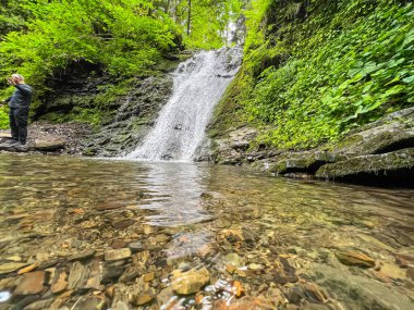 Sahne görkemli bir şelaleyi ihtişamlı bir şekilde yakalar, sanki zamanda donmuşçasına. Kristal berrak su, kayalık bir uçurumdan düşer. Köpüklü beyaz püskürtüsü, etrafındaki arazinin toprak tonlarına zıt düşer..