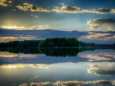 Huzurlu Balık Gölü: tenha bir balıkçı gölünün sakin sularında huzurlu bir manzara. Bereketli yeşilliklerle çevrili ve berrak mavi gökyüzü ile çerçevelenmiş bu resim mükemmel bir günün özünü yakalıyor. 