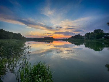 Huzurlu Balık Gölü: tenha bir balıkçı gölünün sakin sularında huzurlu bir manzara. Bereketli yeşilliklerle çevrili ve berrak mavi gökyüzü ile çerçevelenmiş bu resim mükemmel bir günün özünü yakalıyor. 