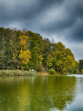 Serene Balıkçı Gölü: Gözlerden uzak bir gölün sakin sularında sakin bir manzara. Etrafı yemyeşil ve bulutlu bir gökyüzü ile çevrili bu resim, mükemmel bir günün özünü yakalar. 