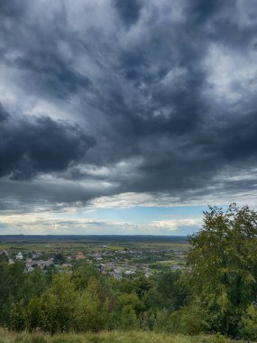 Dramatik bulutlu gökyüzünün altındaki köyün tepe manzarası. Yağmurdan önce kırsal köy manzarası