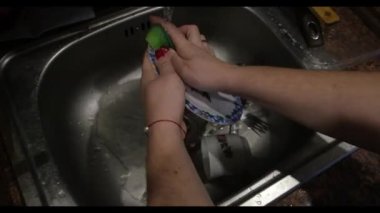 A woman washes dishes, a view from above. Washes a ceramic plate with flowers in a metal ditch. High quality FullHD footage