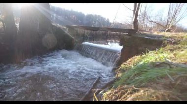 A small waterfall under a small bridge of planks across a mountain river at sunrise6 Water noise. High quality FullHD footage