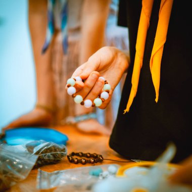 Bir el, DIY atölyesinde renkli boncuklu bir bilezik tutuyor. Detaylı işçilikle kişisel bir aksesuar oluşturuyor.