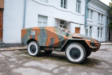 Kamufle edilmiş eski bir zırhlı araç dışarıda park halinde, askeri tasarım ve mühendisliği gösteriyor.