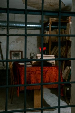 An eerie scene shows a table with deep red fabric, scattered old books, and a haunting, imprisoned backdrop clipart