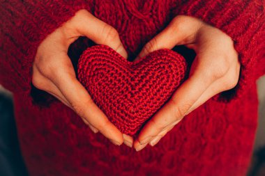 Kırmızı örülmüş kalbi tutan bir kadın. Organ bağışı, aile sigortası. Aşk konsepti, Sevgililer Günü