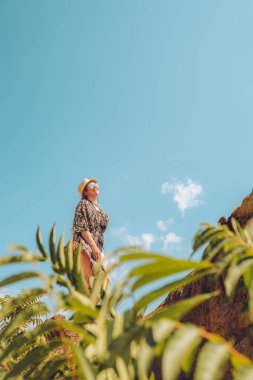 Deniz kenarında şapka ve gözlük takan mutlu kadın yaz havasının tadını çıkarıyor.