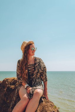 Deniz kenarında şapka ve gözlük takan mutlu kadın yaz havasının tadını çıkarıyor.