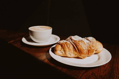 Kafede kapuçino, latte sanatı ve kruvasan.