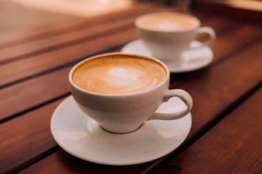 Two cups of cappuccino with latte art on the wooden table. Beautiful foam and ceramic cup