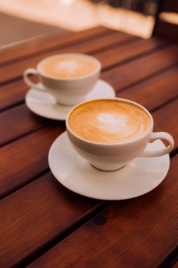 Two cups of cappuccino with latte art on the wooden table. Beautiful foam and ceramic cup