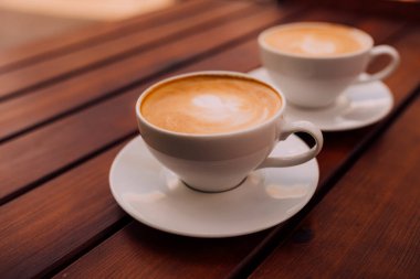 Two cups of cappuccino with latte art on the wooden table. Beautiful foam and ceramic cup