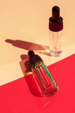 Two glass bottles with cosmetic liquid on bright red background with shadows and light reflections. Flat lay style and close-up. Copy space for your design
