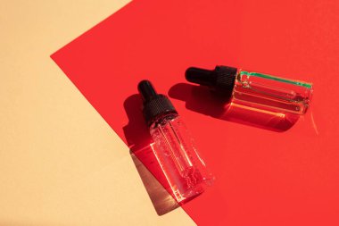 Two glass bottles with cosmetic liquid on bright red background with shadows and light reflections. Flat lay style and close-up. Copy space for your design