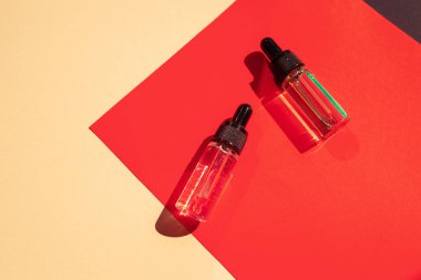 Two glass bottles with cosmetic liquid on bright red background with shadows and light reflections. Flat lay style and close-up. Copy space for your design