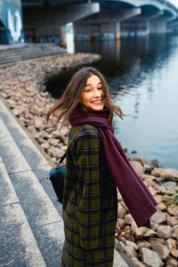 Genç esmer kadın dışarıda yürürken gülümsüyor..