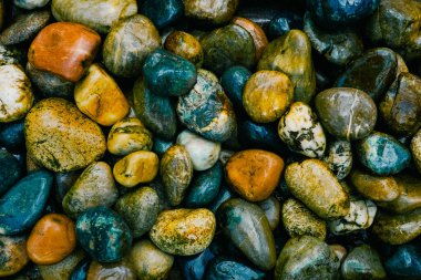 Kıyıda renkli, pürüzsüz taşlar var. Kayalarla dolu bir arkaplan.