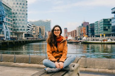 Gülümseyen genç kadın Hafencity, Hamburg, Almanya 'da bankta oturuyor..