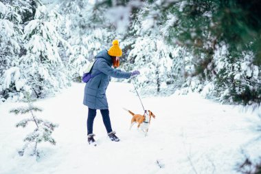 Young woman playing with her beagle dog in snowy winter forest