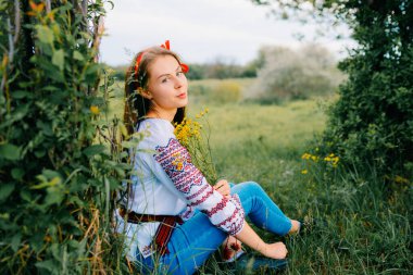Doğada yemyeşil ve sarı çiçeklerle çevrili geleneksel kıyafetli genç bir kadın..