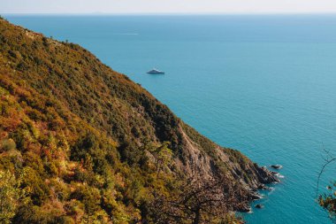 Bu fotoğraf, denizin mavi sularının üzerinde yükselen engebeli bir uçurumun muhteşem manzarasını, İtalyan Riviera 'sının 5 Terre bölgesindeki sahil şeridi boyunca seyreden etkileyici lüks bir yatı gösteriyor. Görüntü bir macera hissi veriyor.