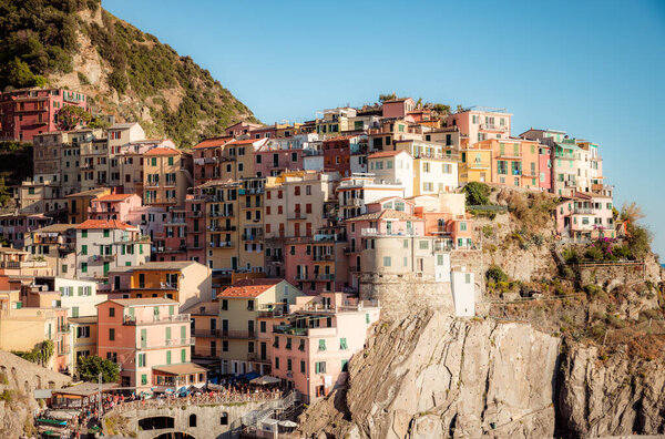 Manarola, a coastal town in Italy, showcasing the colorful houses that line the steep hillsides overlooking the sea, with a small harbor and boats in the foreground, and the blue waters stretching towards the horizon