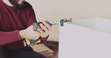 Yetenekli bir adam güçlü bir kablosuz elektrikli tornavida kullanarak evdeki mobilyaları ustalıkla monte ediyor.