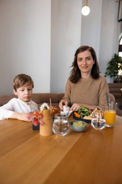 Genç ve şık bir anne ve onun sevimli sarışın oğlu şık bir kafede sağlıklı bir brunch eşliğinde besleyici ve lezzetli yemeklerin tadını çıkarıyorlar. Bu iç açıcı an, şehirde sağlıklı beslenme kavramını yakalıyor.