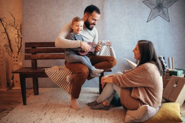 Anne şefkatle izlerken hediyeler ve yanıp sönen ışıklarla çevrili.