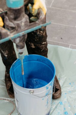 İnşaat işçisi elektrikli mikser kullanarak kovada mavi epoksi reçineyi karıştırıyor.